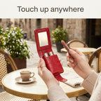 Red lipstick case open with built-in mirror at a cafe table