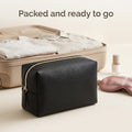 Black makeup pouch in front of a packed suitcase